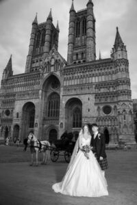 black and white image of bride and groom outside lincoln cathedral with horse and carriage